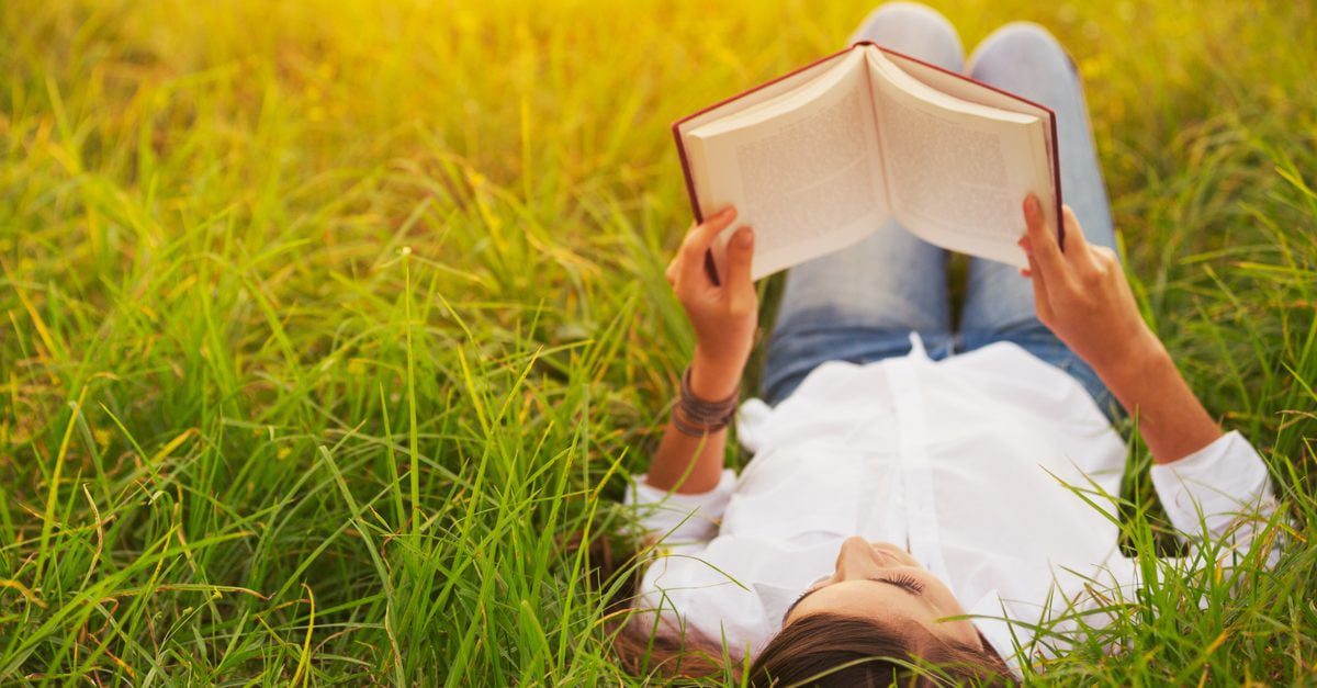 Woman lying on the grass while reading a book.