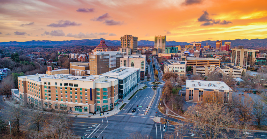 Aerial view of the buildings at Downtown Asheville surrounded by the Appalachian Mountains during a the sunset.