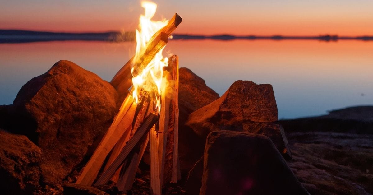 A bonfire by a lake during a red sunset.
