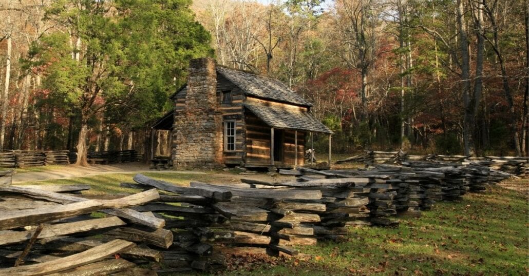 A woord and stone cabin surrounded by big trees during the fall season.