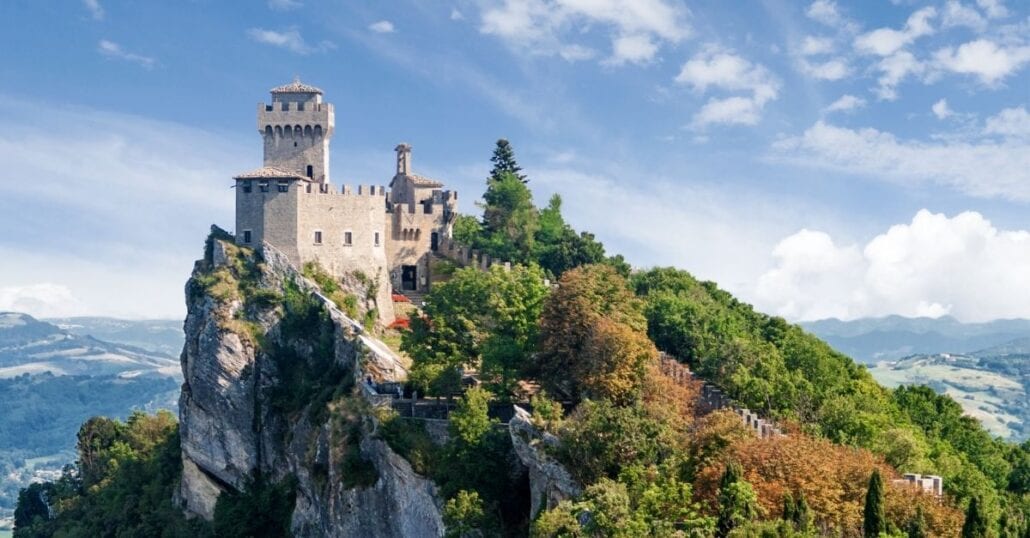 View of the Three Towers of San Marino over a green forested hill.