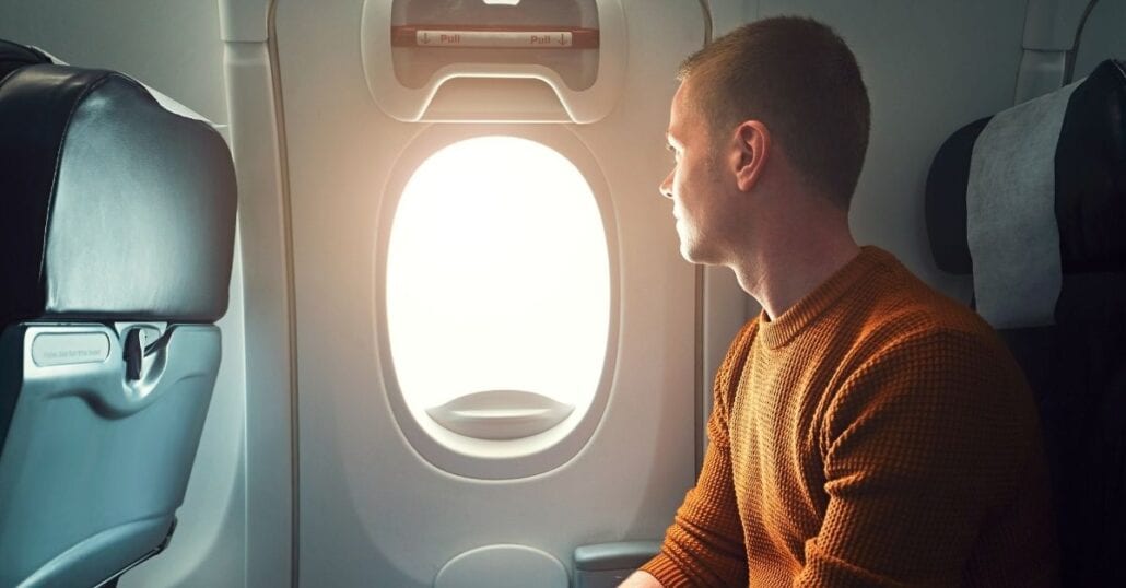 A young man looking through the window on an airplane during the day.