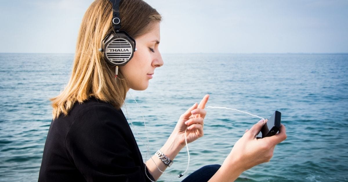 Woman listening to a travel podcast in front of the ocean.