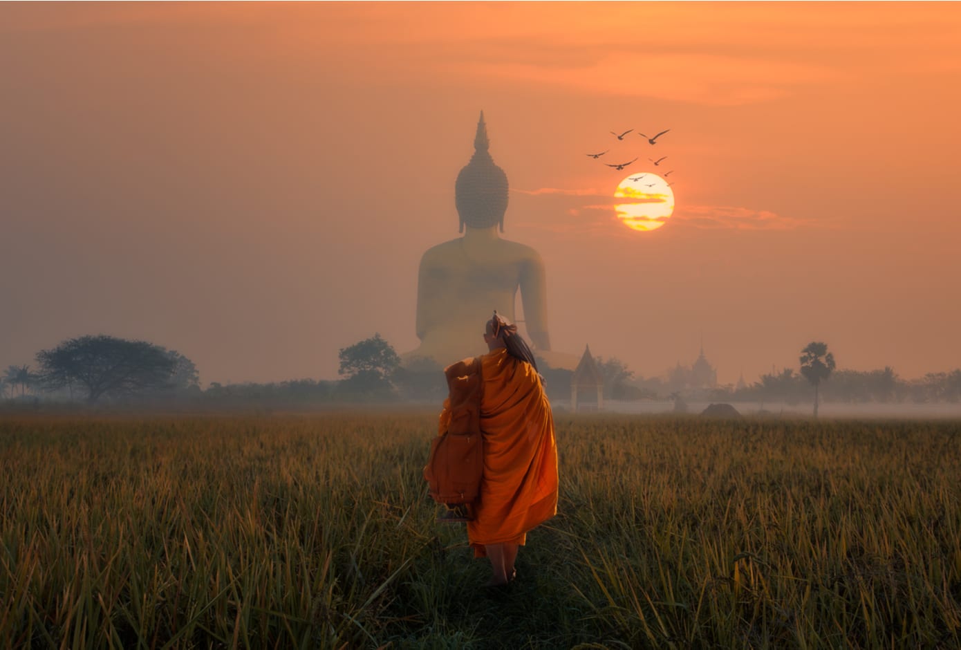 Monk walking towards the Big Buddha at Wat Muang Angthong, Thailand Temple at sunset.