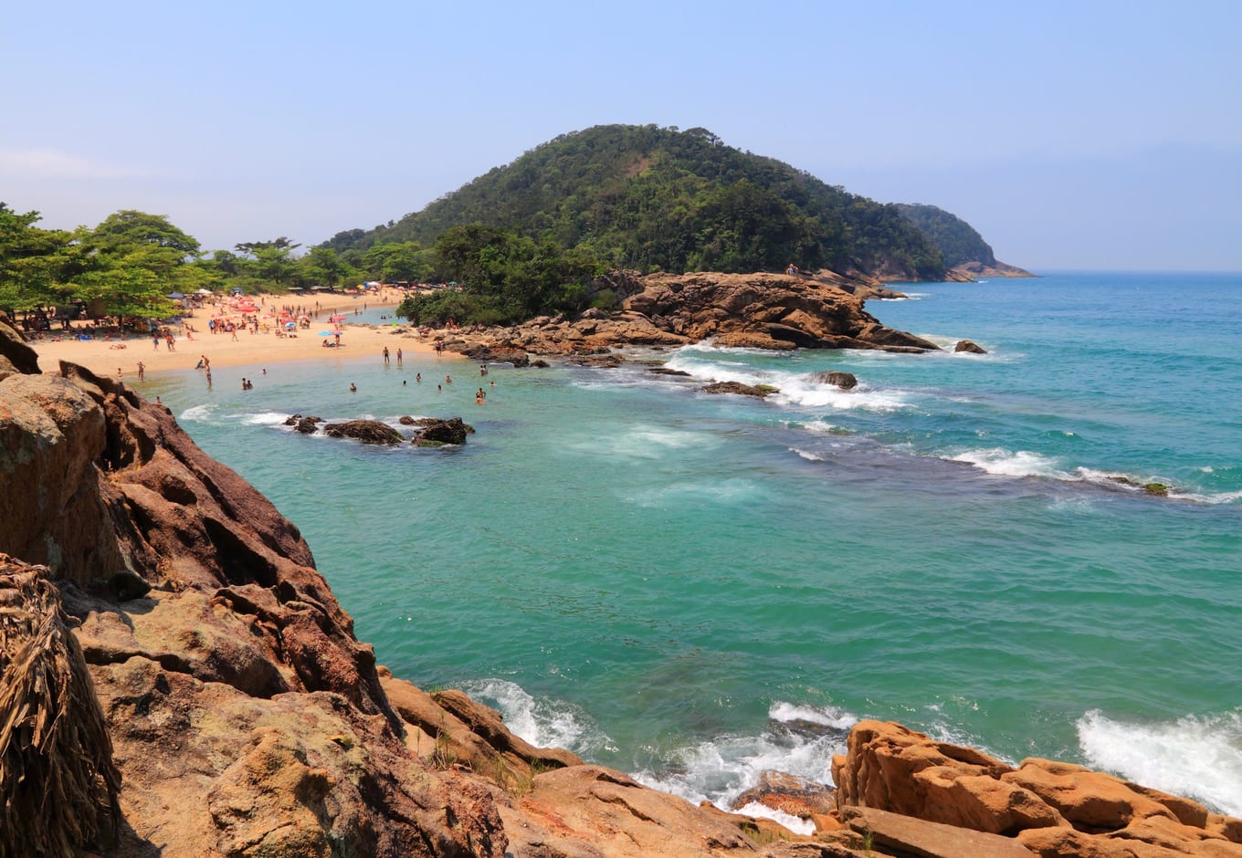 The blue-green ocean surrounded by rocks and a forested hill on Trindade Beach, Brasil.
