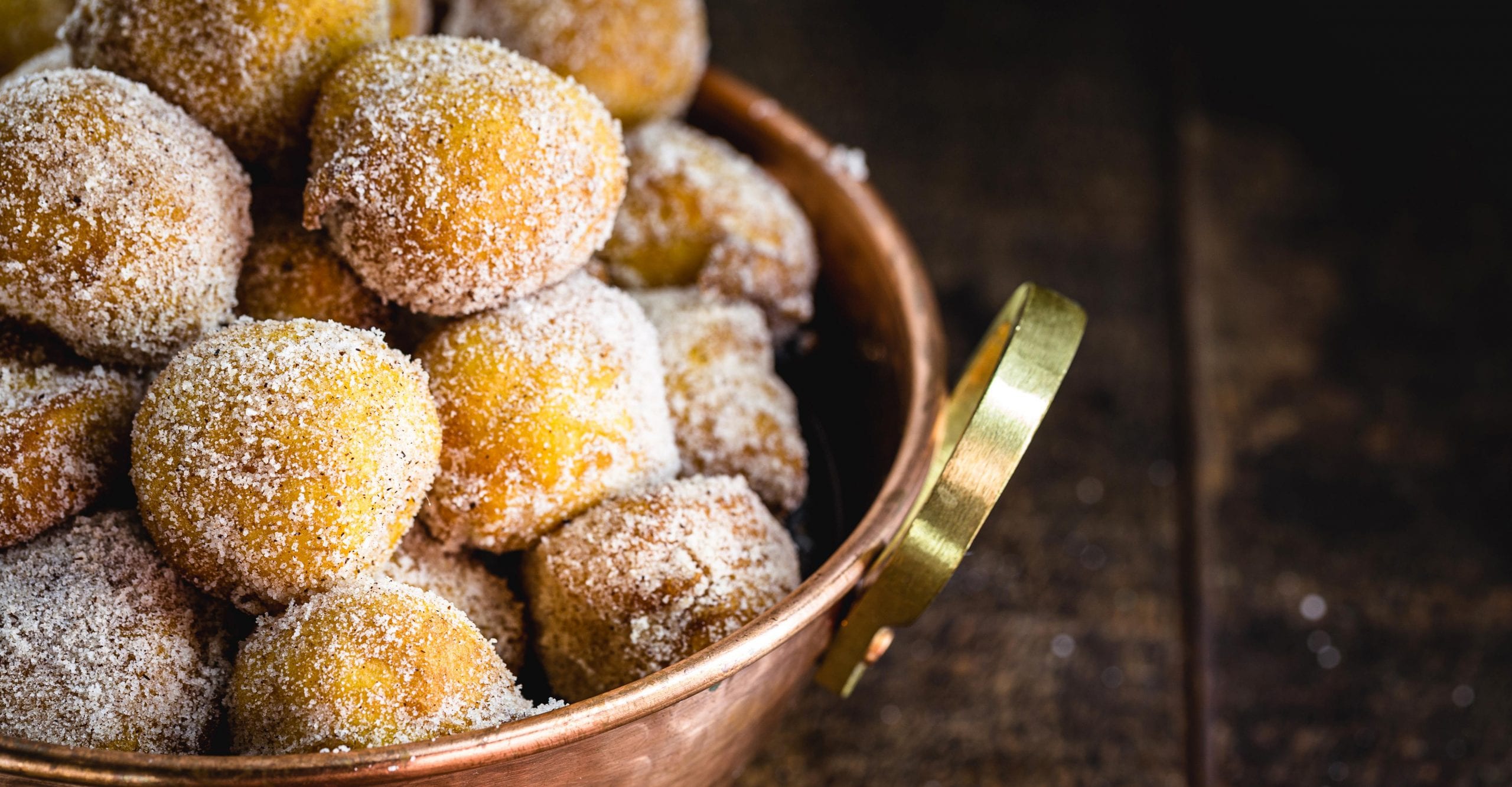 A copper bowl filled with Croatian fritules with powdered sugar on top.