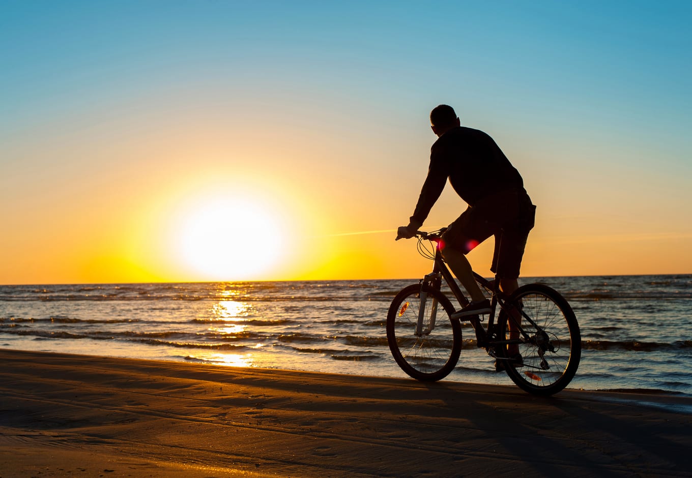 A man cyclist on the beach during the sunset. 
