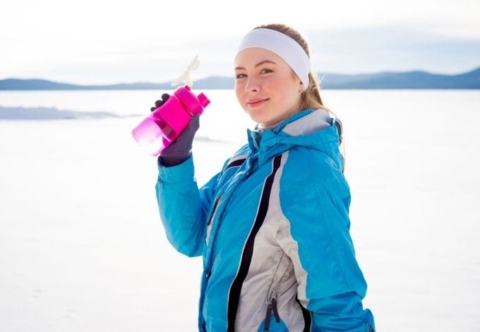 Young woman drinking water on a snowy mountain.