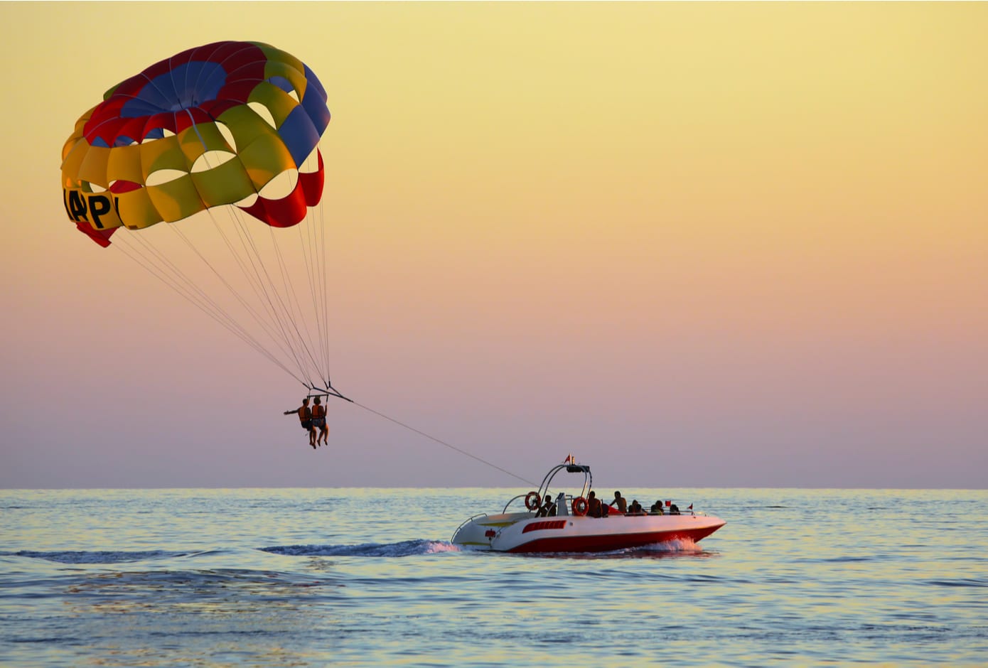 Two people parasailing above the ocean at sunset.