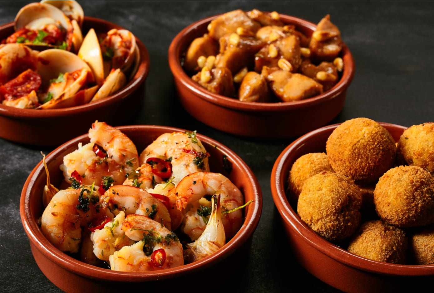 Four red ceramic bowls filled with Spanish tapas.