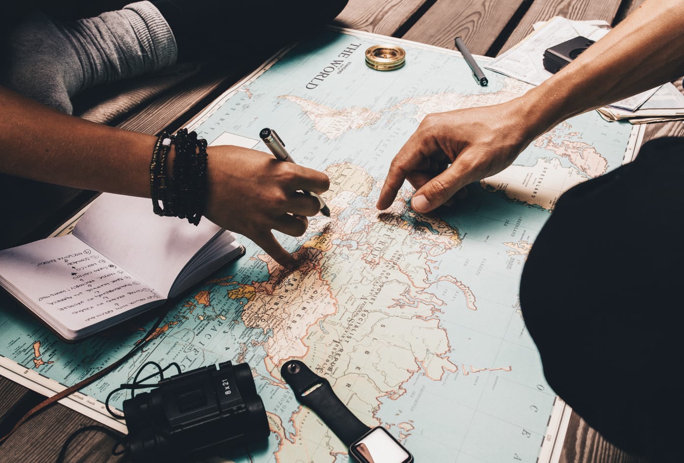 Two travelers pointing at a map and taking notes while planning a trip.