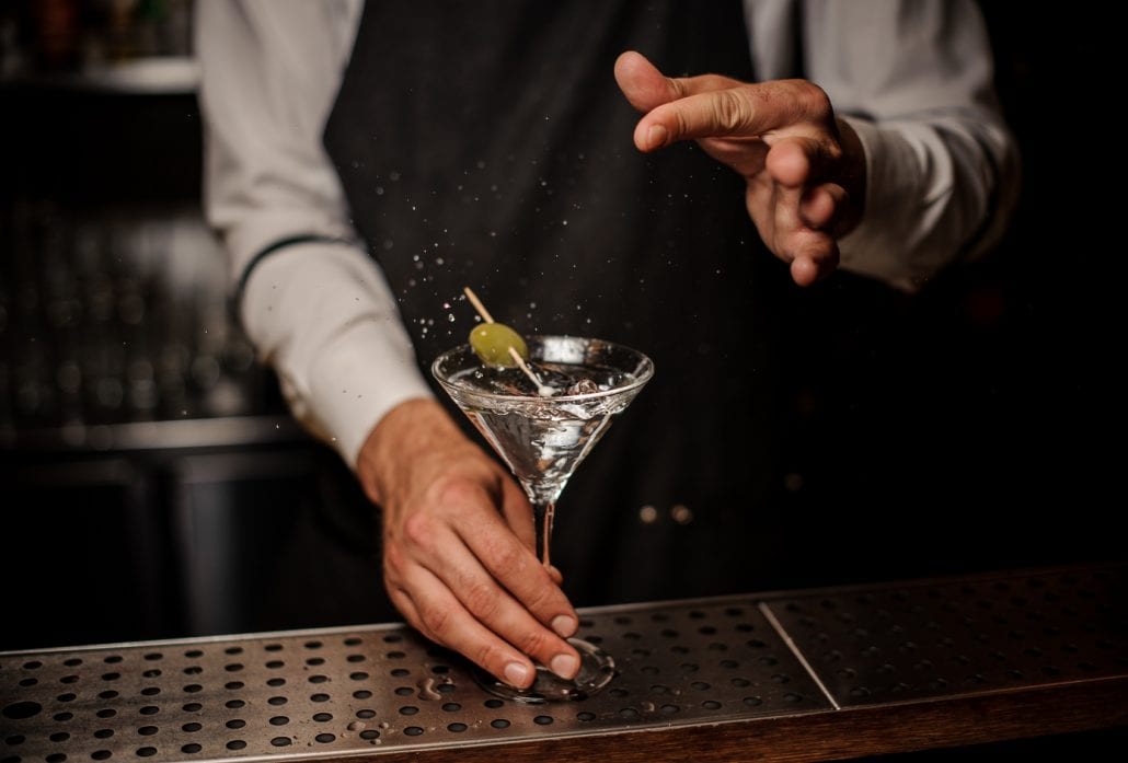 Bartender making a martini cocktail with a green olive and salt
