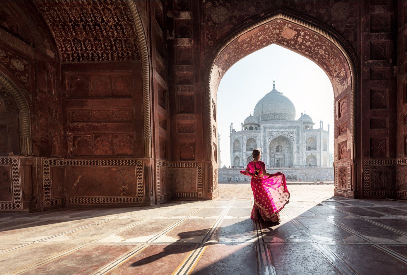 Woman with flowy red dress facing the Taj Mahal, in India.