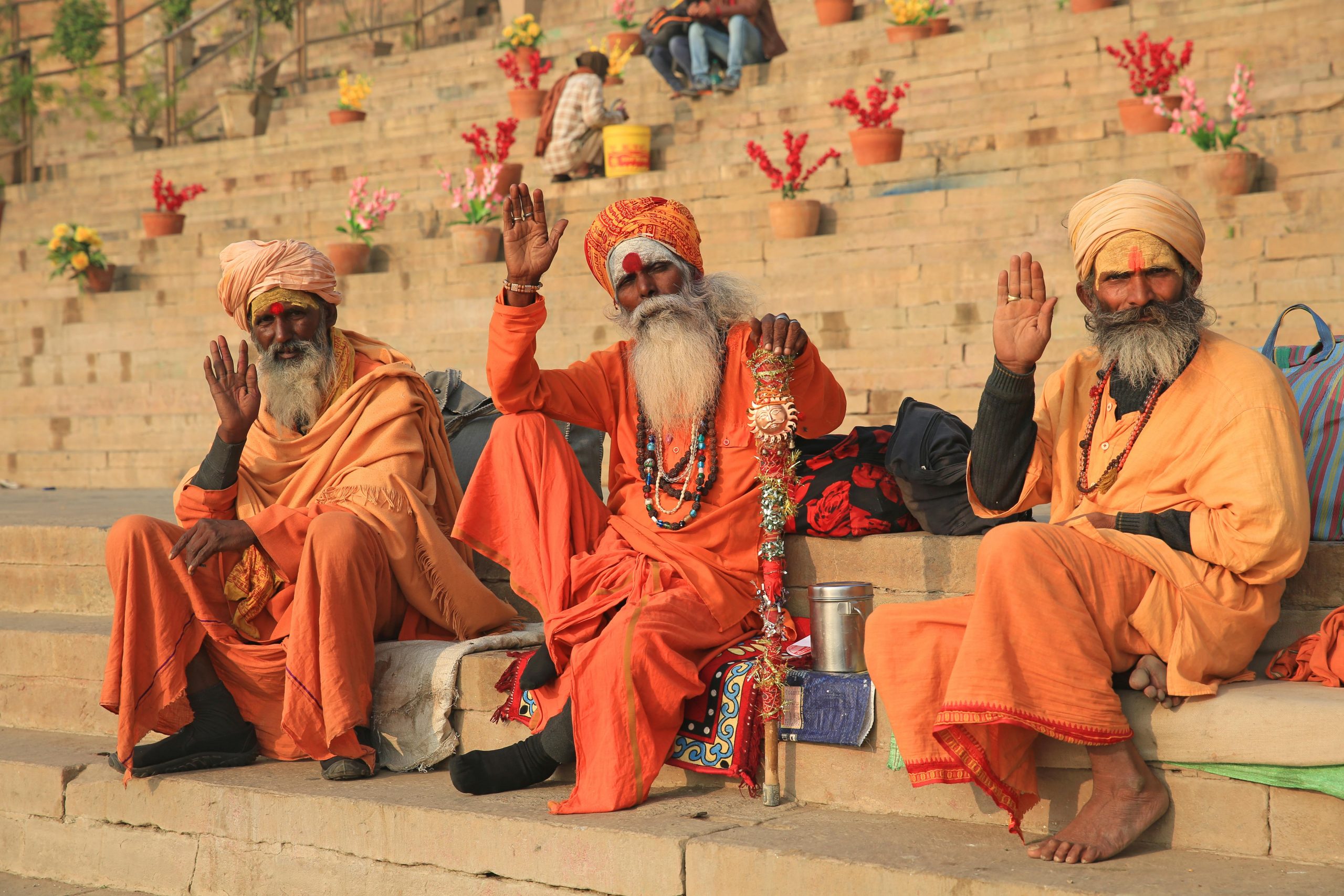 Three Hindu ascetics wave while sitting on the steps leading down to the sacred Ganges River in Varanasi, India