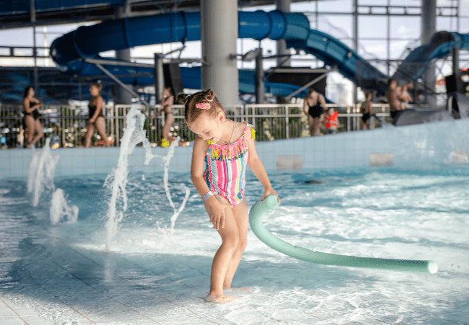 Little beautiful girl playing with a foam noodle in a indoor pool. rest in the water park