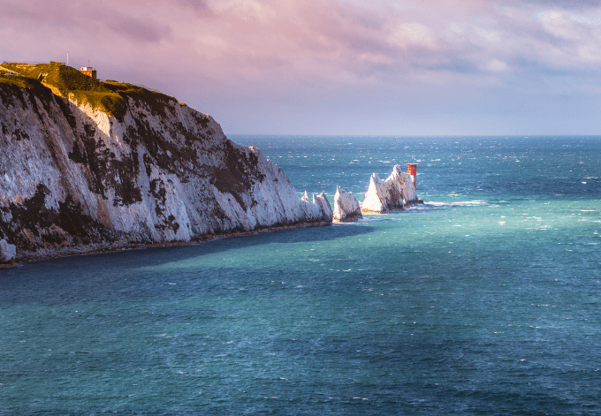 A break in the clouds illuminates the iconic chalk stone pinnacles of The Needles and the 19th century lighthouse on the coastline Isle of Wight an island off the south coast of England.