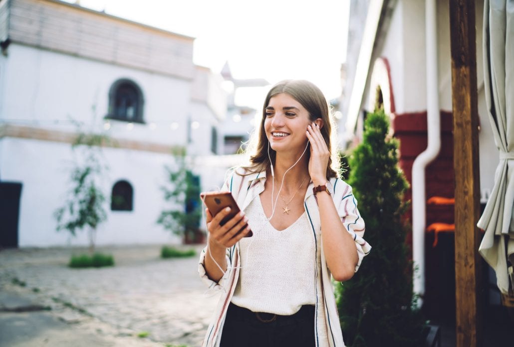 Smiling girl in earphones listening to music on her smartphone.