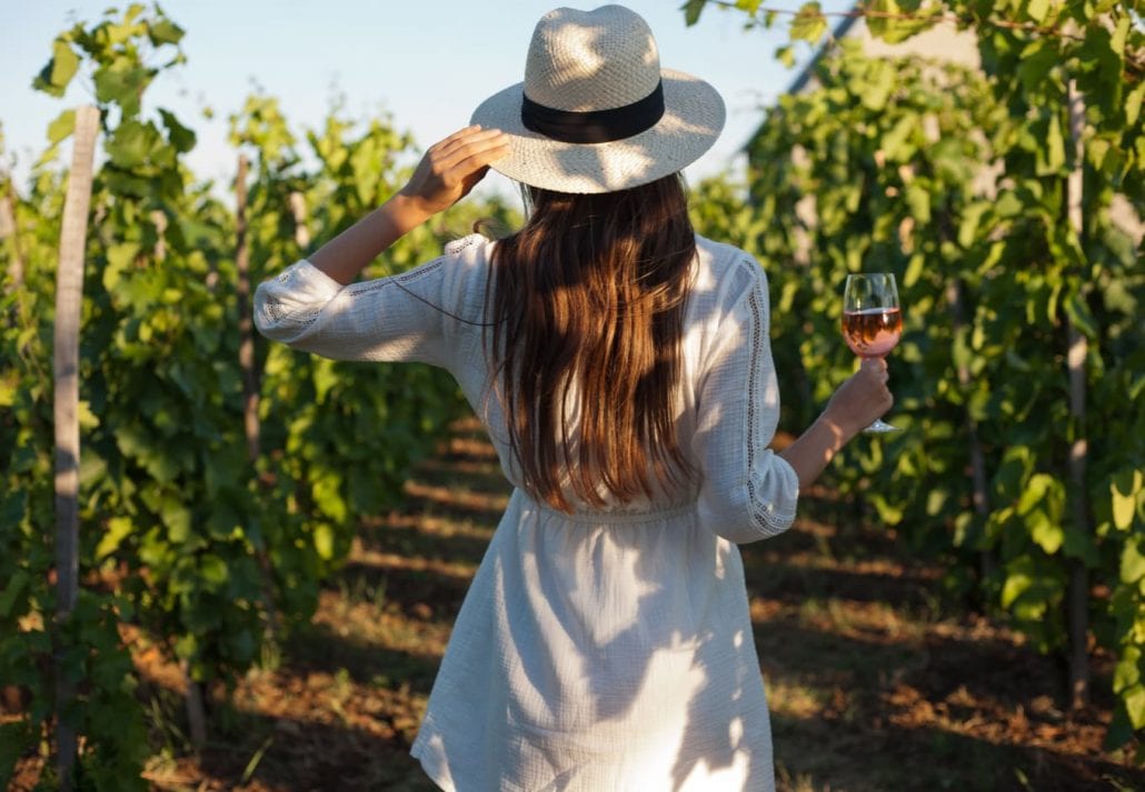 Woman drinking rose while walking on a vineyard.