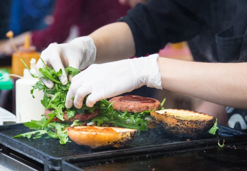 Close up a person's hands filling a burger with arugula at a street food stall.