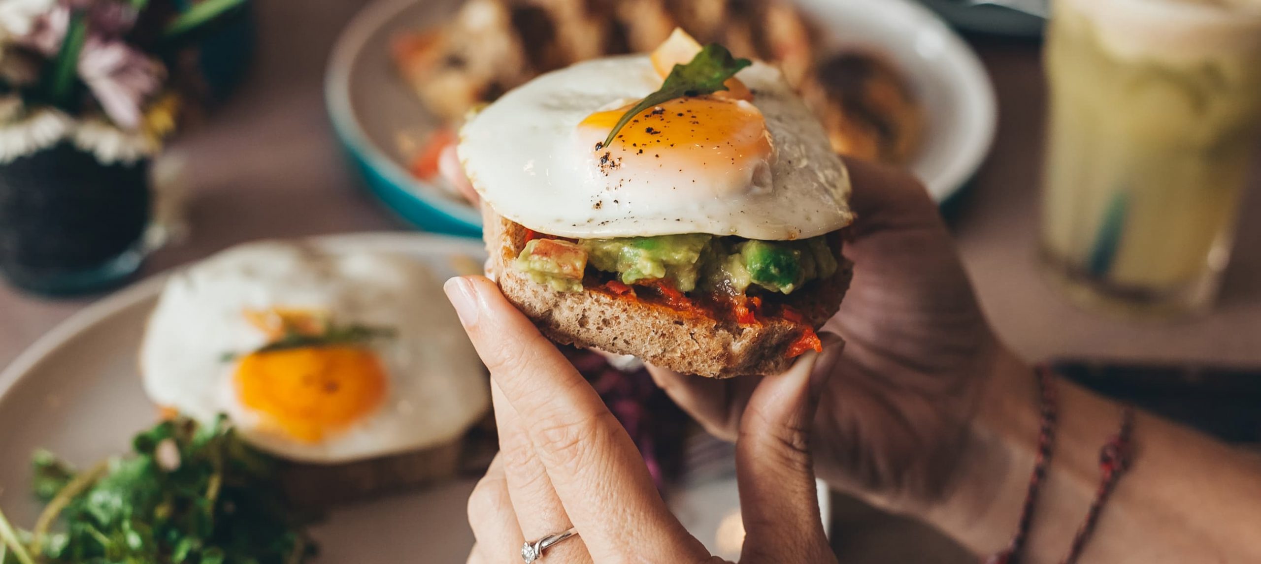 Female hands holding avocado toast with egg during brunch.
