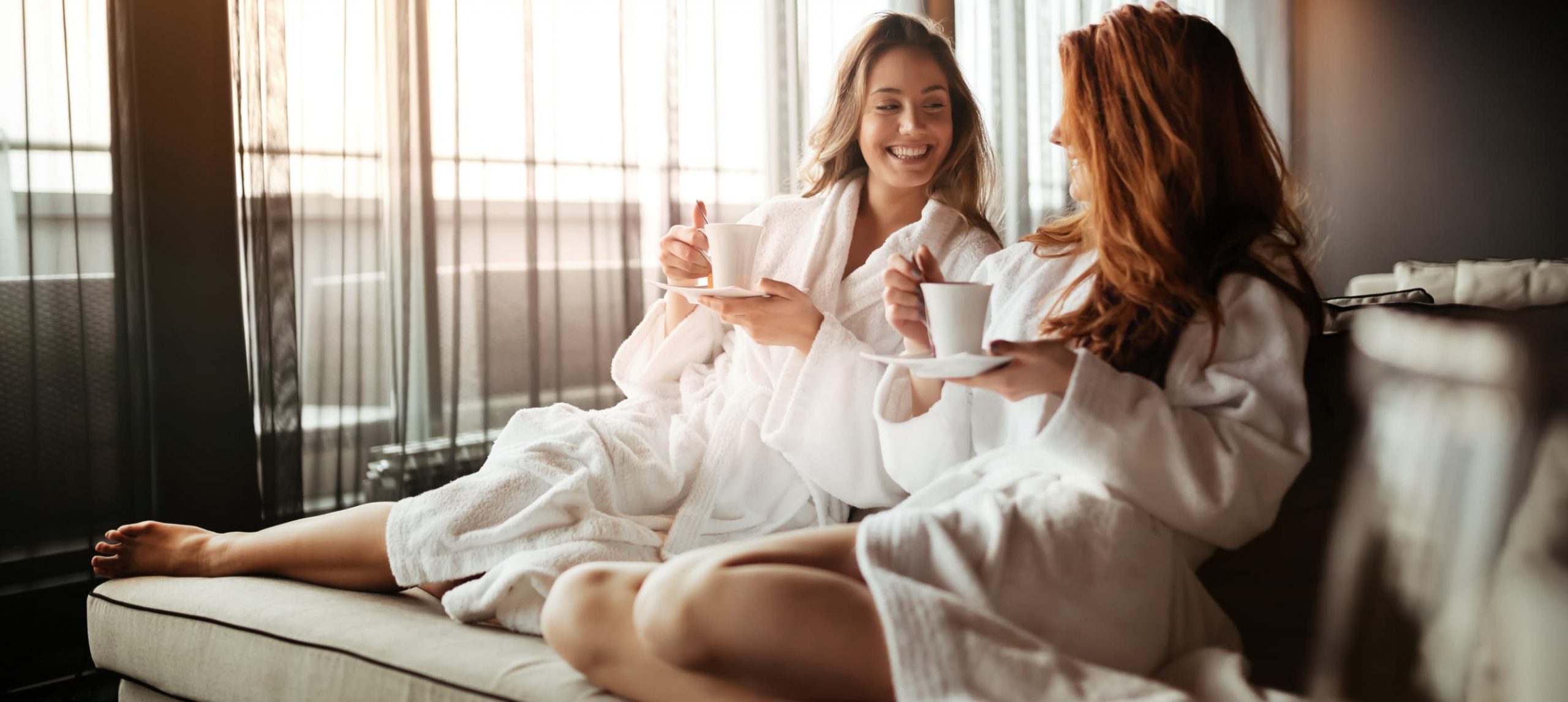 Two females smiling at each other with tea in their hands at a spa retreat