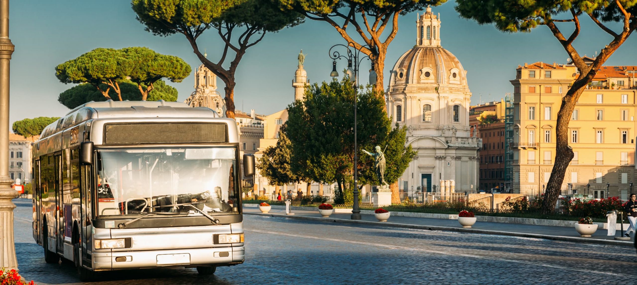 Public City Bus At Bus Stop In Via Dei Fori Imperiali Street In Sunny Summer Morning. View On Church Of Most Holy Name Of Mary.