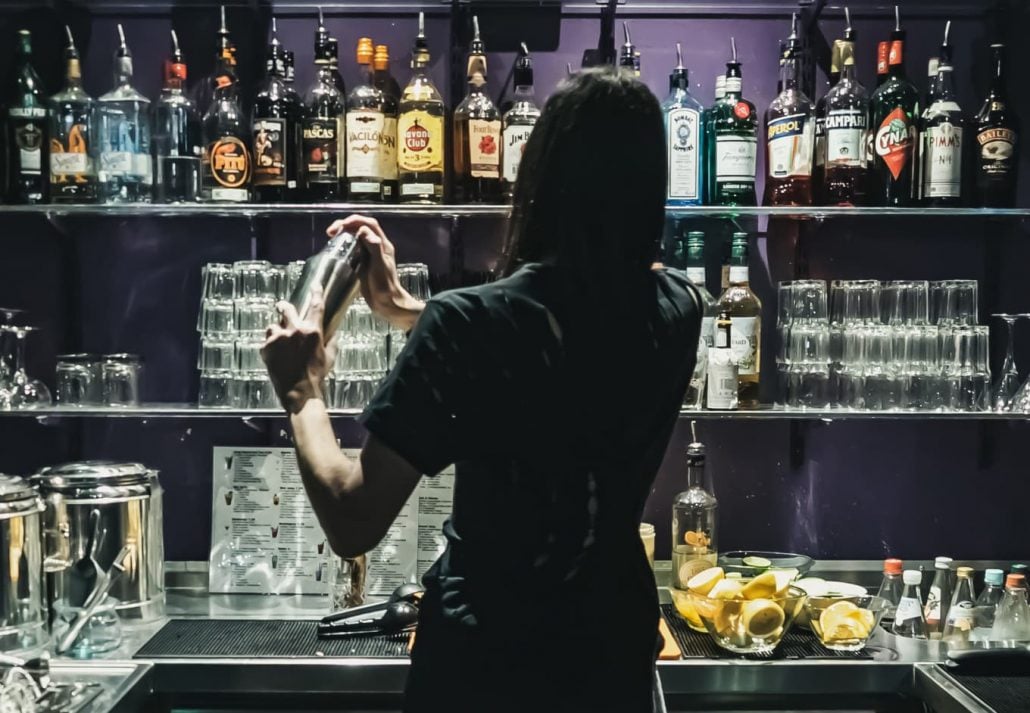 A mixologist creating a cocktail in front of shelfs full of drinks in Monster Ronsons Ichiban Karaoke