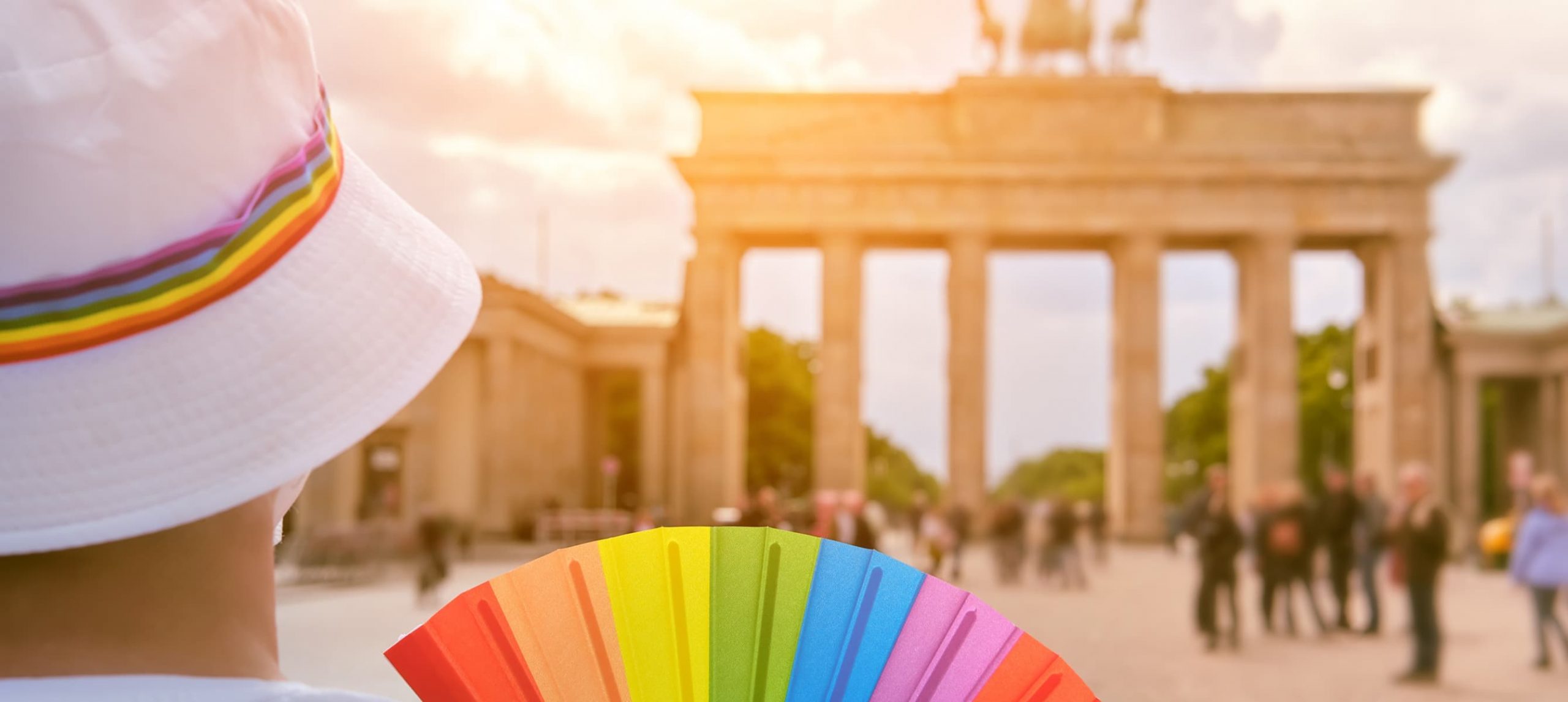 A person in rainbow colors looking at the Brandenburg Gate