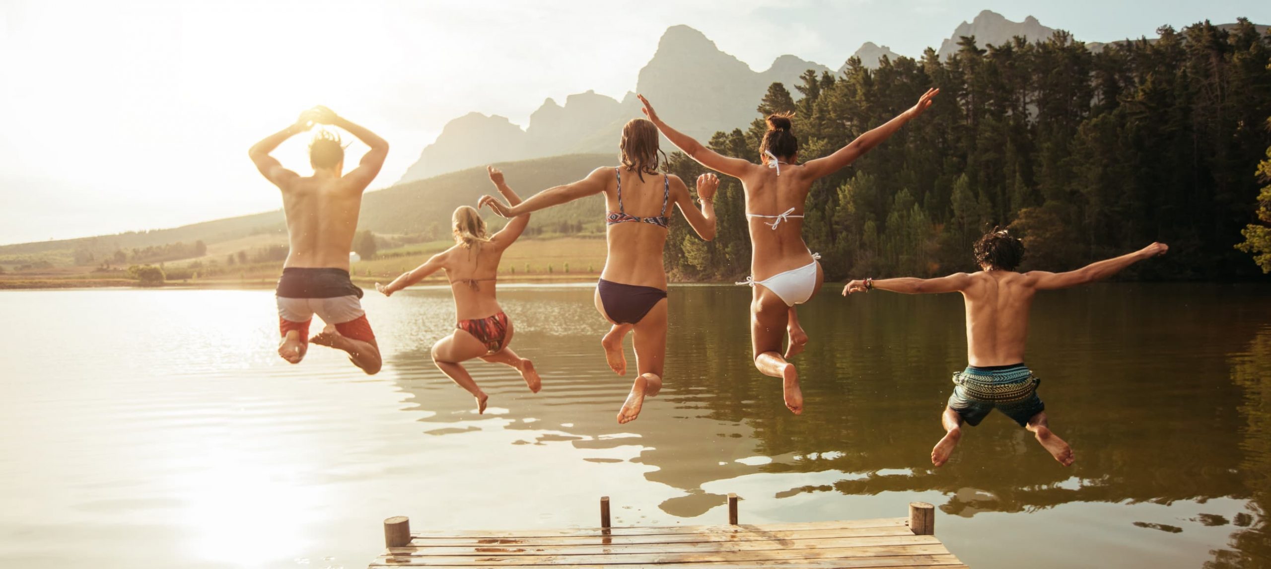 Group of 5 friends happily jumping in a lake.