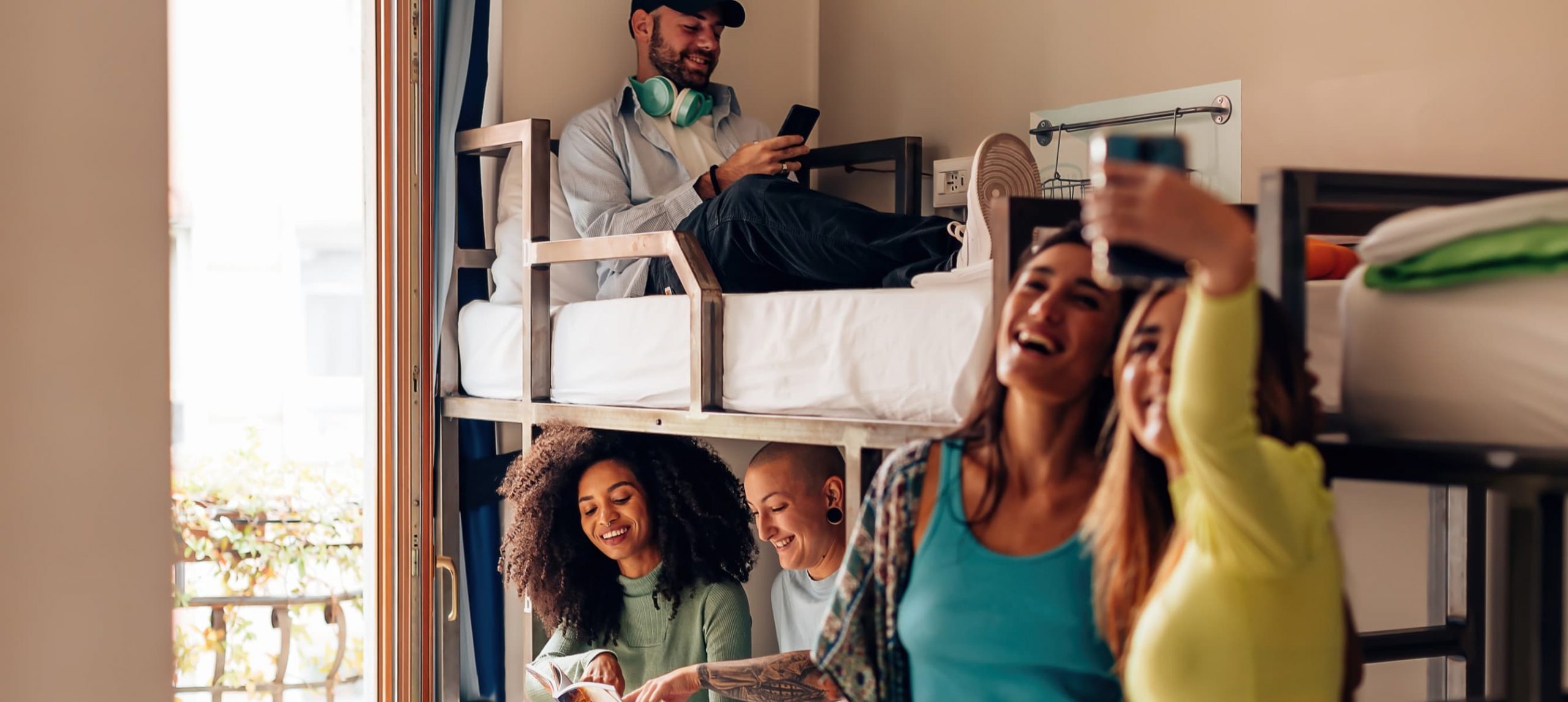 Young travelers happily chatting in a hostel bedroom.