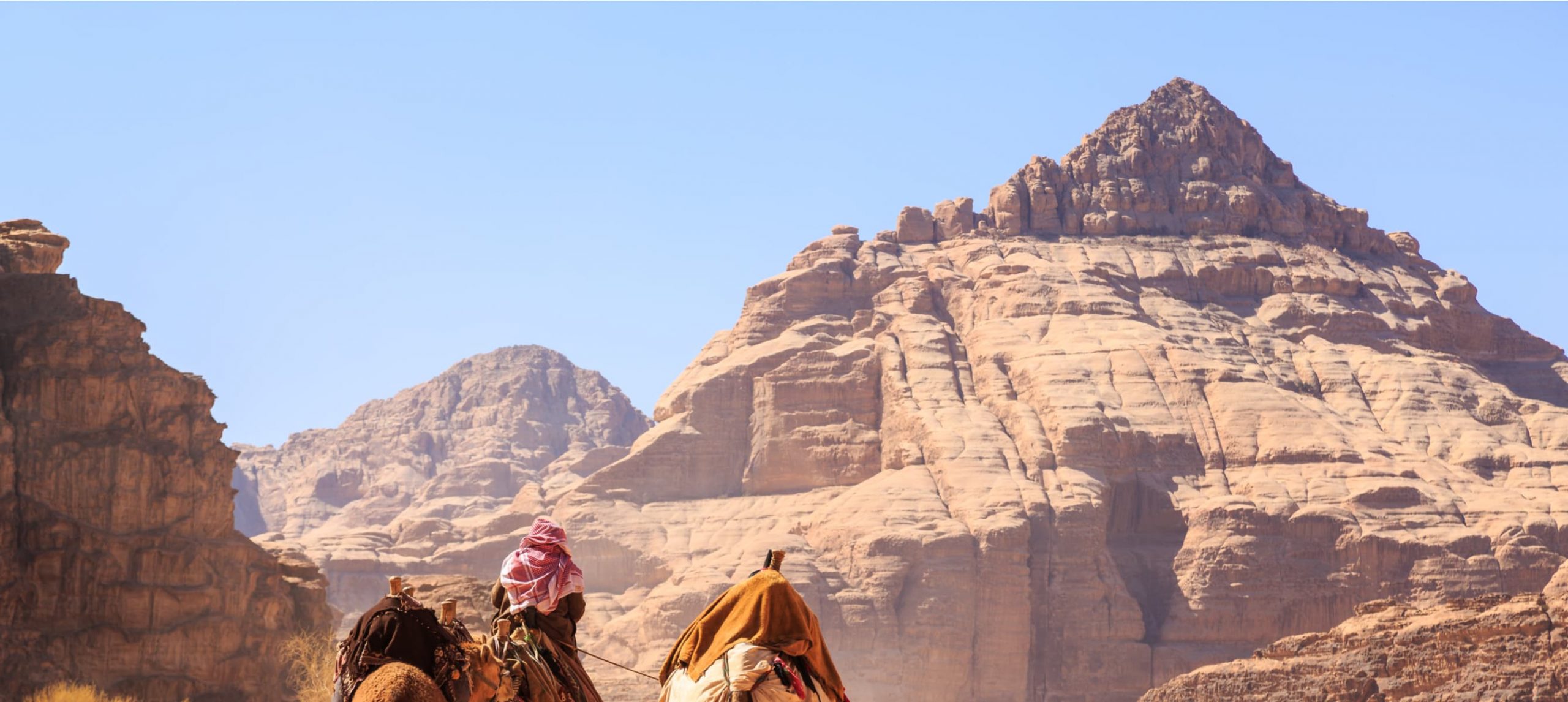 Wadi Rum mountains and two males riding a camel in Jordan