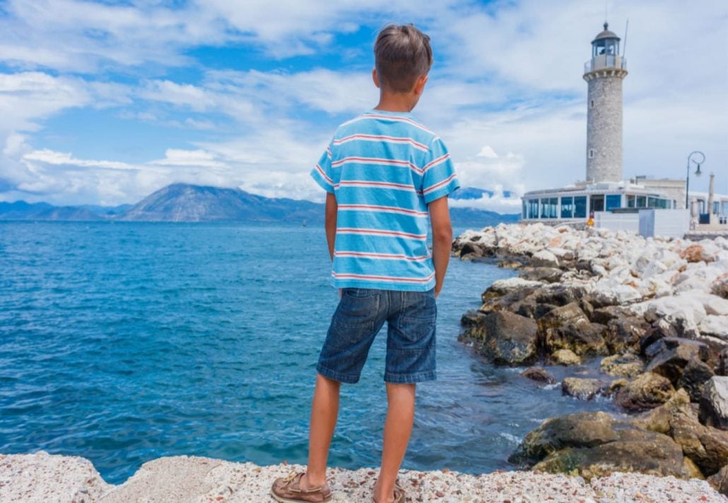A boy standing and looking at the lighthouse by the shore