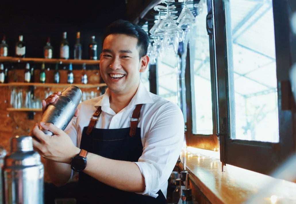 A mixologist making a drink and smiling at a camera