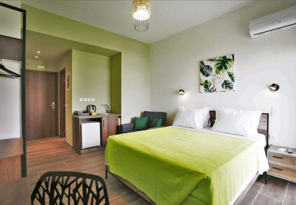 A hotel room with a green bed, a wall picture of leaves, and wooden flooring