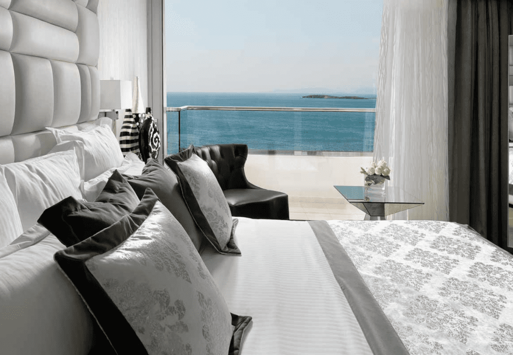 A luxurious hotel room with white bedding and a sea view balcony