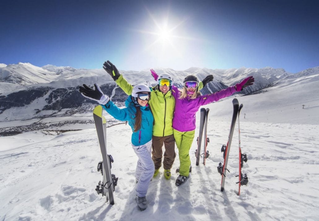 Three people posing for a photo with skis at the mountain peak