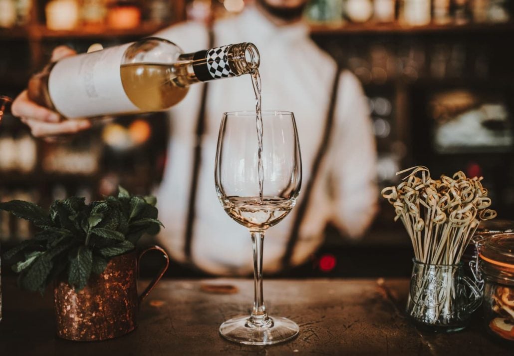 A bartender pouring white wine in a glass
