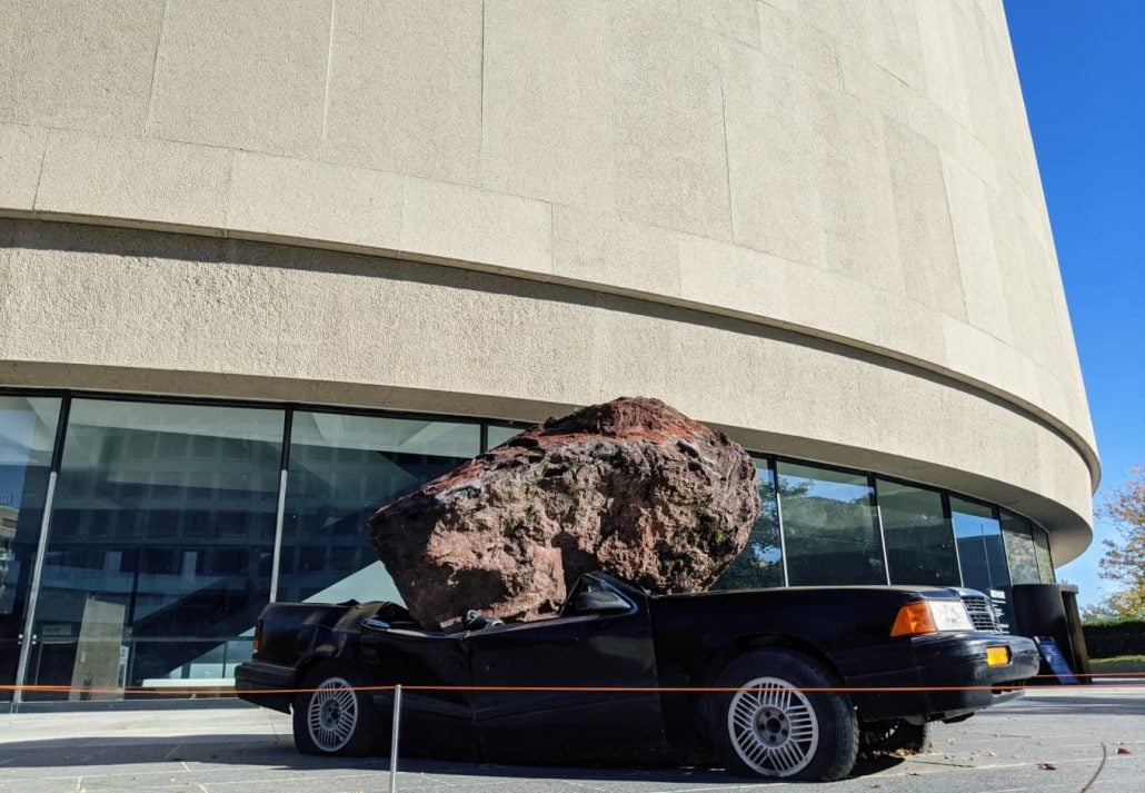 a massive rock on top of a black car in front of the Hirshhorn Museum