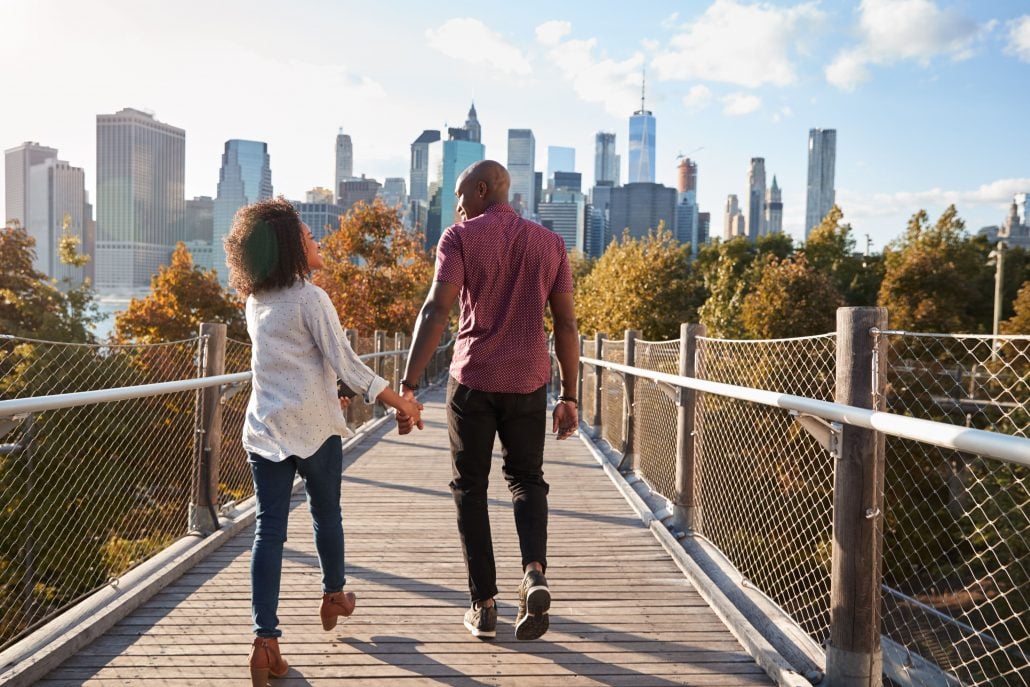 A happy couple crossing a wooden bridge in Manhattan while laughing and holding hands.