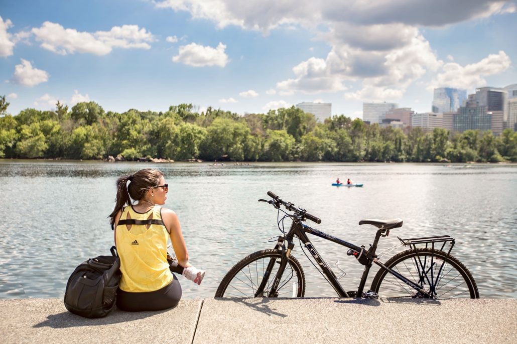 a girl sitting next to a bike in front of the river
