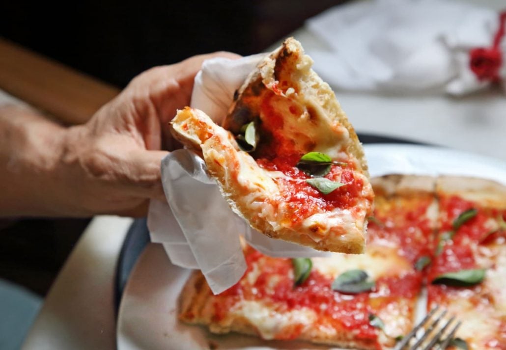 A male hand holding a slice of New York style pizza.