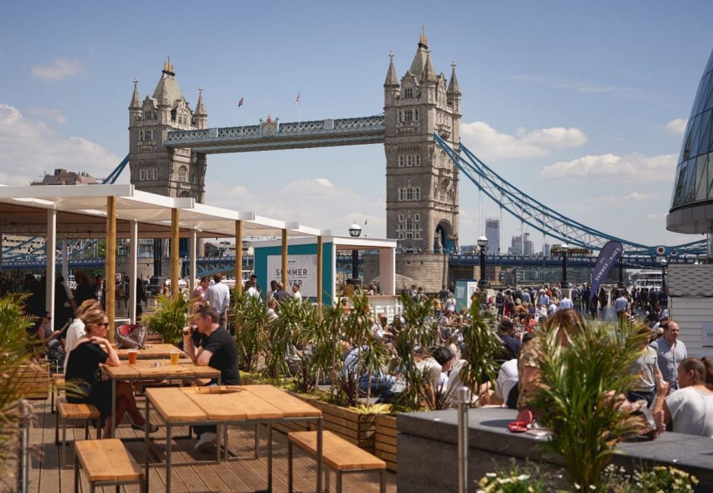 A rooftop bar filled with people, and offering views of the Tower Bridge of London.